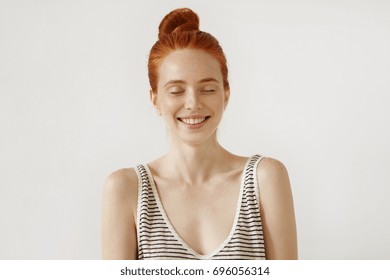 Redhead pretty girl with freckled skin, closing her eyes with happy expression, smiling broadly, anticipating to recieve present from her boyfriend. Ginger young woman waiting for pleasant surprise