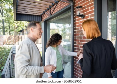 Redhead Realtor Showing Modern House To Happy Multiethnic Couple