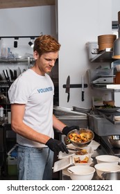 Redhead Social Worker In Latex Gloves Holding Bowl With Prepared Food Near Plastic Containers