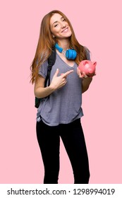 Redhead student woman holding a piggybank on isolated pink background