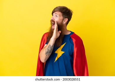 Redhead Super Hero man isolated on yellow background shouting with mouth wide open to the lateral