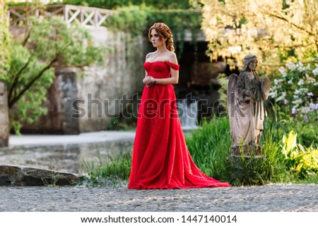 Redhead tattoed woman in red dress near the castle