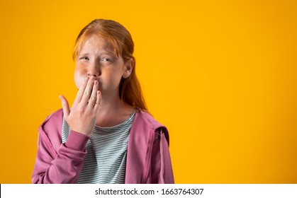 A redhead teenage girl with freckles on her face covers her mouth using her hand while feeling nauseated and with the urges to vomit. Concept for upset stomach, viral infection, gastric problems