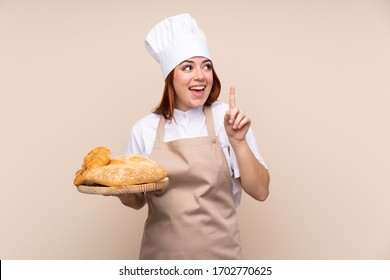 Redhead teenager girl in chef uniform. Female baker holding a table with several breads intending to realizes the solution while lifting a finger up - Powered by Shutterstock