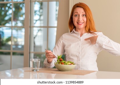 Redhead woman eating fresh green salad at home with surprise face pointing finger to himself - Shutterstock ID 1139854889