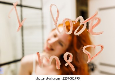 Redhead woman lipstick on the mirror and look at herself feeling confident self love. Love me true ...Inscription I LOVE ME - Powered by Shutterstock