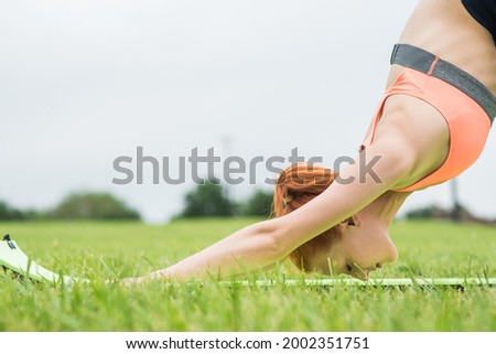 Redhead woman practicing yoga on a mat in summer in the park