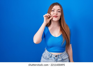 Redhead Woman Standing Over Blue Background Mouth And Lips Shut As Zip With Fingers. Secret And Silent, Taboo Talking 