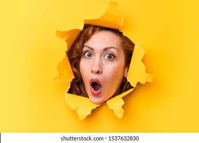 Redhead woman through a hole paper making surprise gesture