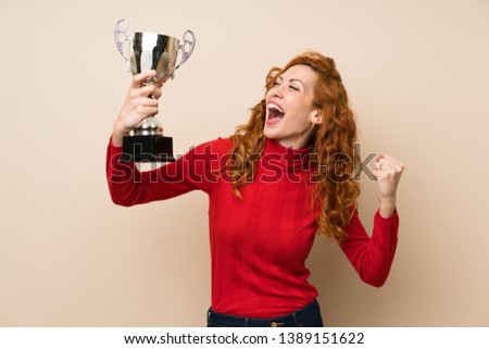 Redhead woman with turtleneck sweater holding a trophy