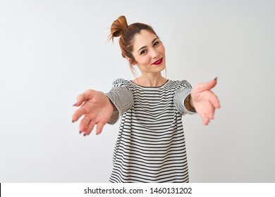 Redhead woman wearing navy striped t-shirt standing over isolated white background looking at the camera smiling with open arms for hug. Cheerful expression embracing happiness.