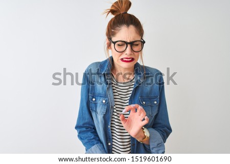 Redhead woman wearing striped t-shirt denim shirt and glasses over isolated white background disgusted expression, displeased and fearful doing disgust face because aversion reaction