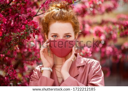 Redhead woman wearing trendy fashion pink monochrome outfit with luxury designer protective face mask. Close up portrait. Vogue, street style during quarantine of coronavirus outbreak. 