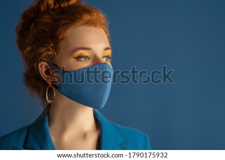 Redhead woman wearing trendy fashion blue monochrome outfit with  protective face mask. Model has matching bold eyes makeup. Style during quarantine of coronavirus outbreak. Copy, empty space for text