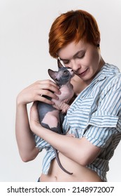 Redhead Young Woman With Closed Eyes Gently Hugs Cat Looking At Owner. Studio Shot On White Background. Portrait Beautiful Hipster With Short Hair Dressed In Striped White-blue Shirt. Part Of Series.