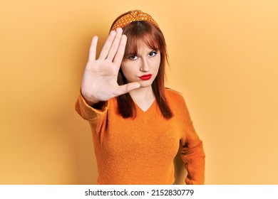 Redhead young woman wearing casual orange sweater doing stop sing with palm of the hand. warning expression with negative and serious gesture on the face. 