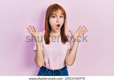 Redhead young woman wearing casual pink t shirt celebrating crazy and amazed for success with arms raised and open eyes screaming excited. winner concept 