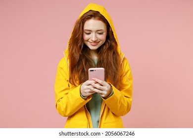Redhead young woman in yellow waterproof raincoat hood outerwear hold mobile cell phone chat online isolated on pastel pink background studio Outdoors lifestyle wet fall cold weather season concept. - Shutterstock ID 2056067246