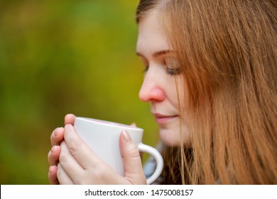 Redheaded Girl With A Red Nose Drinking Hot Tea From A White Mug.  Sick Woman And Autumn