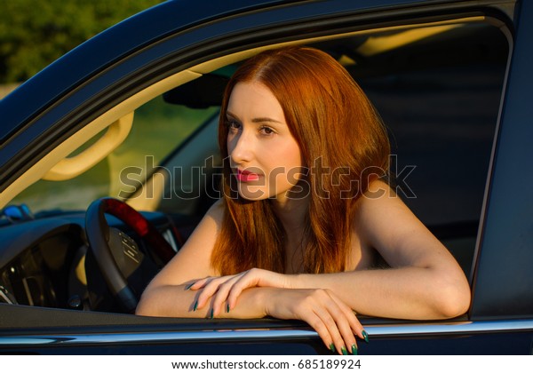 Redheaded young girl\
in the car behind the wheel on the road, road adventure events on\
the road and women\
driving