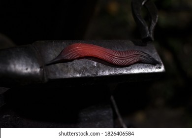 Red-hot Red Feather Of A Bird Forged By Hand On A Metal Anvil. Concept Of Rare Handmade, Dark Colors