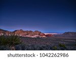 redrock canyon at night with las vegas nevada lit up behind rocks