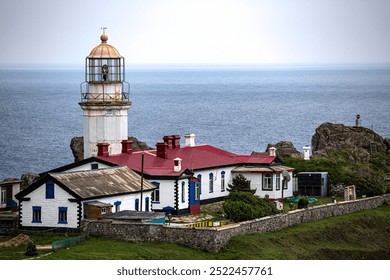A redroofed lighthouse is on a hill by the ocean