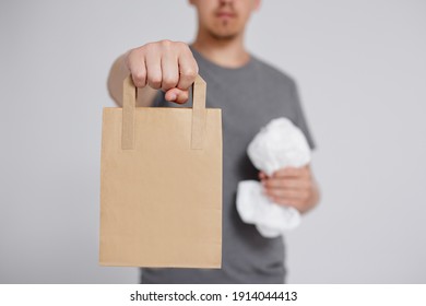 reduce, reuse and recycle concept - plastic bag and brown recyclable eco-friendly paper bag in male hands over grey background