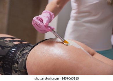reducing the volume of the hips with the help of special cosmetic products, applying a special cream on the buttocks of the girl, Spa treatments in the cosmetologist's office