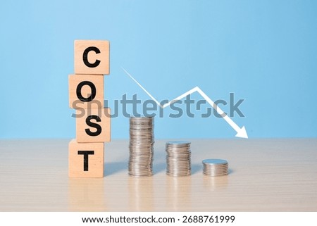 For reduction concept which effect to product cost , profit , inflation and economy recession concept, COST text on wooden cube blocks, stack of coins and decreasing graph