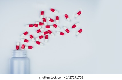 Red-white antibiotic capsule pills spread out of white plastic drug bottle. Antibiotic drug resistance concept. Antibiotic drug use. Global healthcare. Pharmacy background. Pharmaceutical industry.