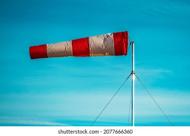 Red-white windsock against the blue sky in sunny weather. Wind vane indicates the strength and direction of the wind