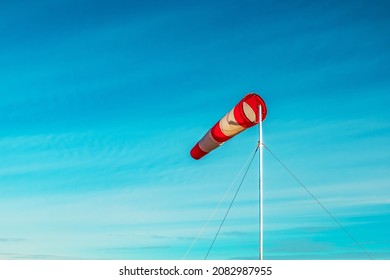 Red-white windsock against the blue sky in sunny weather. Wind vane indicates the strength and direction of the wind
