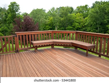 Redwood stained deck boards with a bench seat overlooking the trees in the back yard of a residential home.