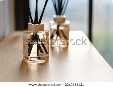 Reed Diffuser in glass bottle placed on wood table against window with gauze curtain in the sunset light. essential oil. brown and gold color. perfume. warm, soft, dreamy, romantic, fashion, luxury