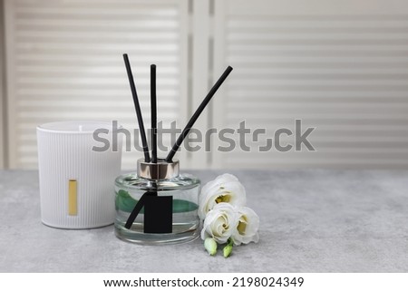 Reed diffuser, scented candle and eustoma flowers on gray marble table, space for text