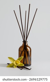 Reed diffuser with vanilla sticks in a brown glass bottle and vanilla flower on light background. Minimal composition symbolizing calmness, purity, and natural aroma.