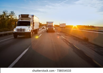 Reefer truck and pickup truck on the road at sunrise with lens flare