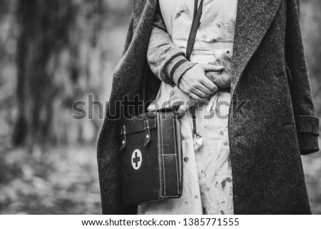 Re-enactor Wears Historical German Nurse Paramedic Of World War II Uniform With First Aid Kit. Photo In Black And White Colors. WWII WW2.