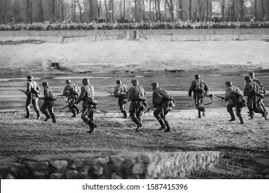 Re-enactors Dressed As German Wehrmacht Infantry Soldiers In World War II Running In Attack In Summer Day. Photo In Black And White Colors.