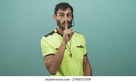 Referee man points finger and makes shushing gesture, whistle on lanyard and headset mic visible in studio; authority command.