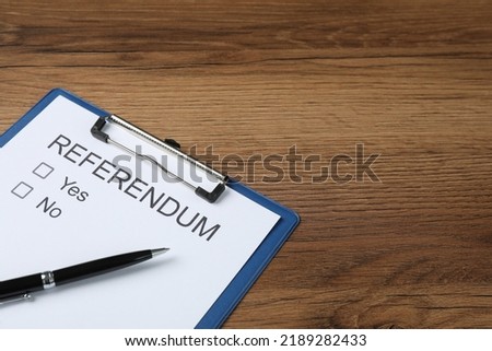 Referendum ballot with clipboard and pen on wooden table. Space for text
