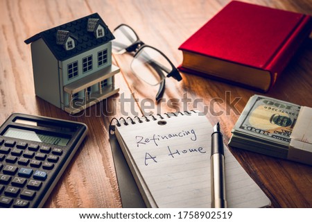 refinancing words on notebook with us dollars and stuff on wooden desk.