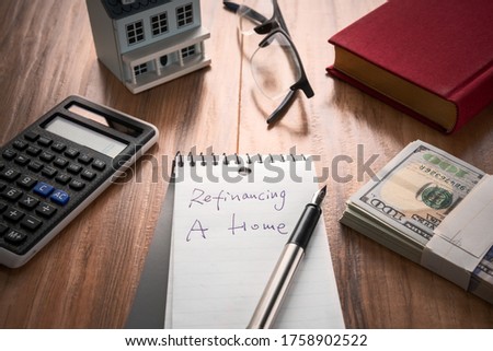 refinancing words on notebook with us dollars and stuff on wooden desk.