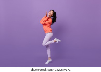 Refined Asian Woman Standing On One Leg. Full Length View Of Blissful Chinese Girl Dancing On Purple Background.