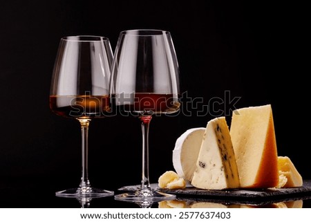 A refined selection of aged cheeses presented on a board, accompanied by a glasses of wine, set against a dramatic dark background. A perfect setting for a gourmet indulgence