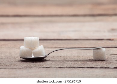 The refined sugar in cubes in a tea spoon on a wooden table from old boards. - Powered by Shutterstock