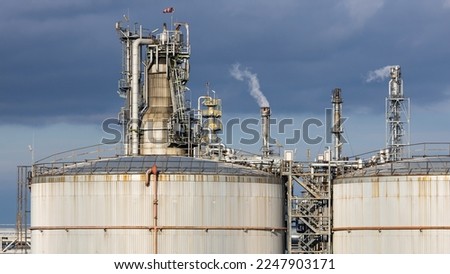 Refinery complex with fuel storage tanks, smokestacks and pipes with dark clouds