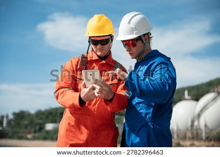Refinery Engineers using tablet at oil terminal during petrochemical industry inspection and offshore energy operations near storage facility.