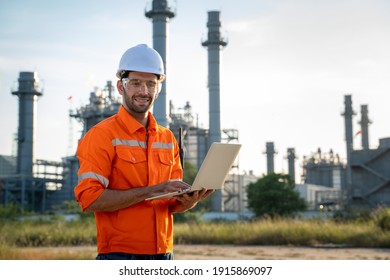 Refinery industry engineer working on computer laptop against oil refinery background.